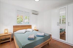 Ein Schlafzimmer mit einem hölzernen Bett, zwei Nachttischen mit Lampen, einem Kleiderschrank und einem Fenster mit Blick auf Grünflächen.