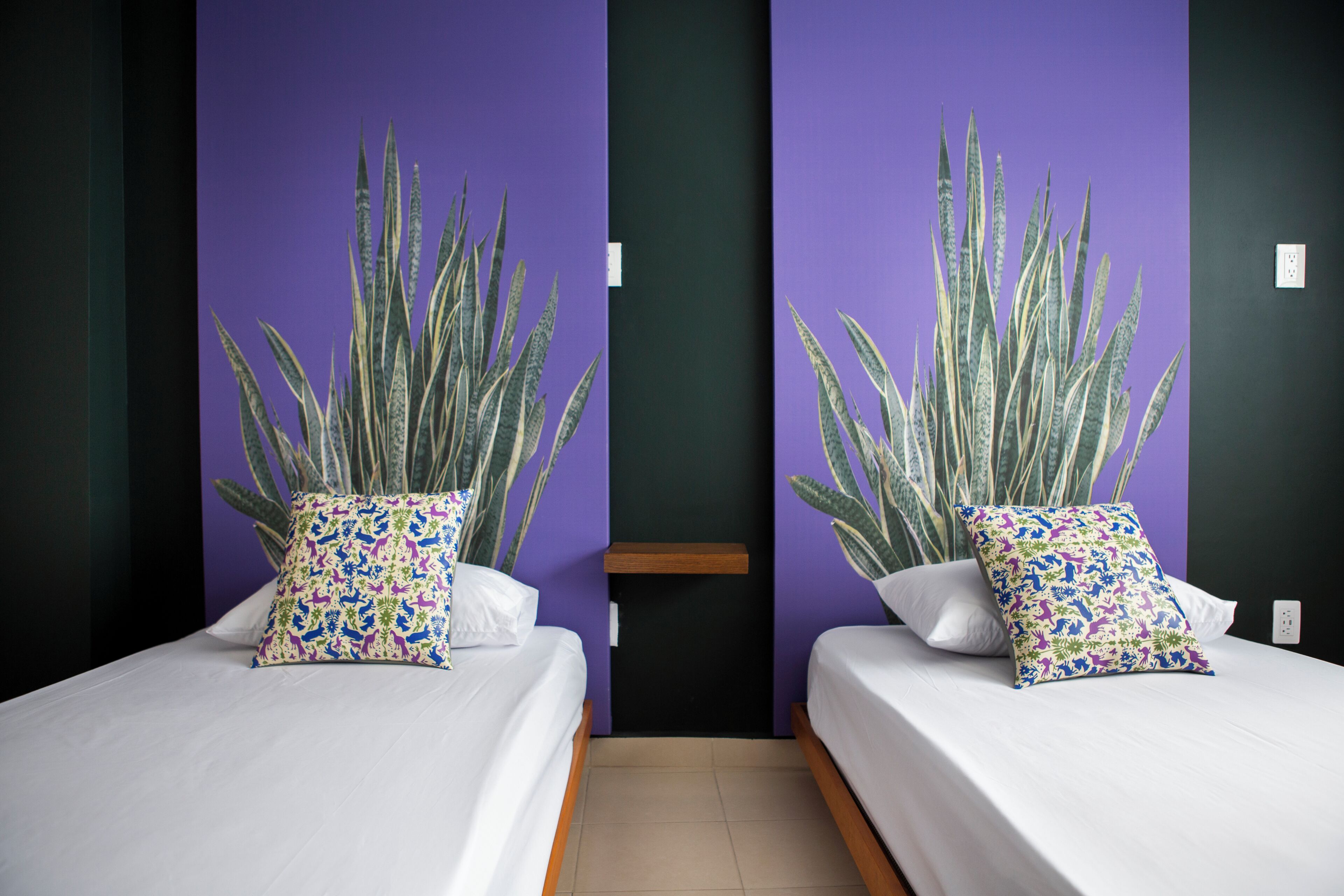 Une chambre avec deux lits, chacun agrémenté d’une grande plante en pot et d’un coussin à motifs.