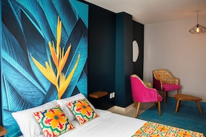 A hotel room with a large wall mural, a bed with colorful pillows, a chair with a patterned cushion, and a unique light fixture. - Casa Local Mestizo Hostal (Mexico City)