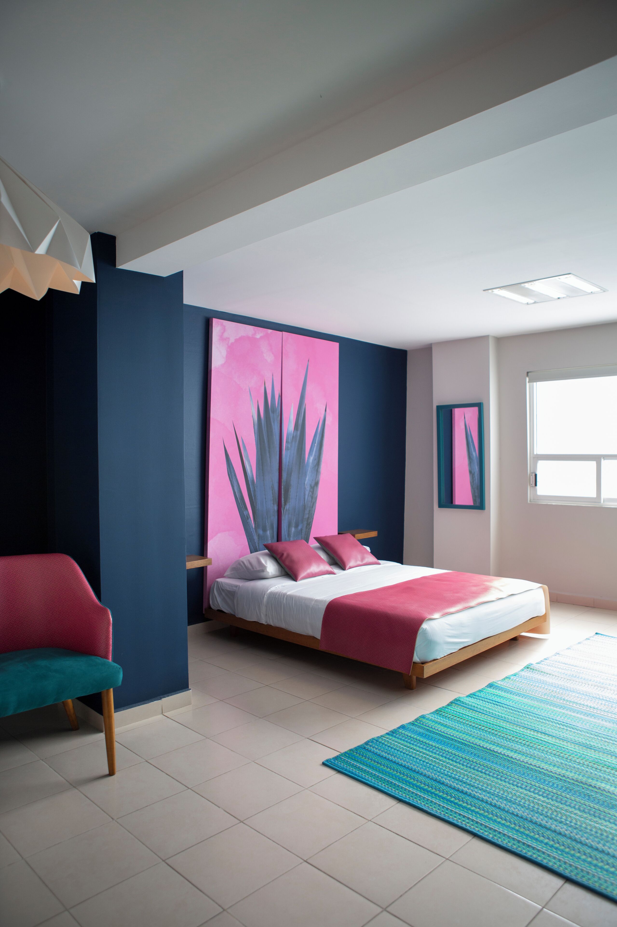 A modern bedroom with a bed, a chair, a large painting, and a window.