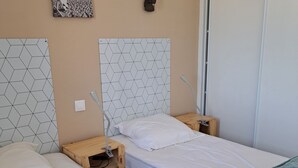 Ein Hotelzimmer mit zwei Einzelbetten, einem Holfnachtkästchen, einem Beistelltisch, einer Wandleuchte und einem gerahmten Bild.
