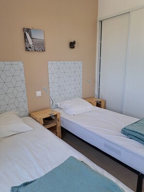 Ein Hotelzimmer mit zwei Einzelbetten, einem Holfnachtkästchen, einem Beistelltisch, einer Wandleuchte und einem gerahmten Bild.