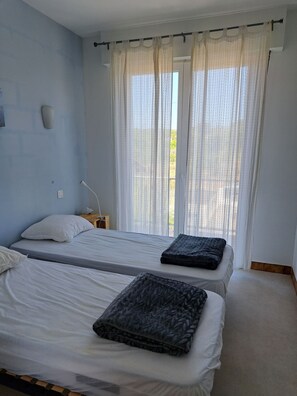 A room with two beds, a nightstand, and a window with sheer curtains. - Between the Sea and Clape: 1st-floor apartment with ocean views, 50 meters from the beach (Narbonne)