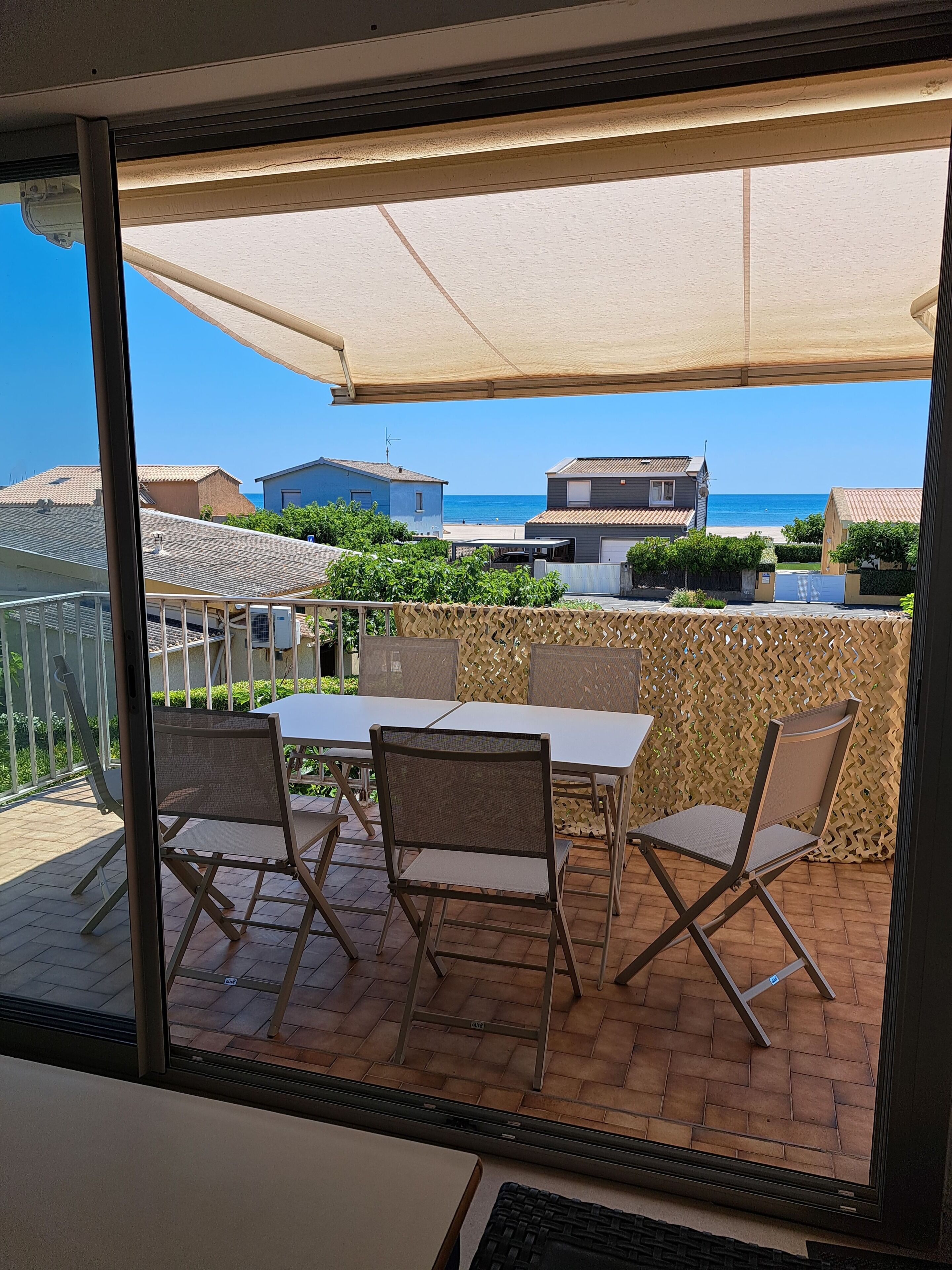 A patio with a table and chairs, overlooking a beach and residential buildings.