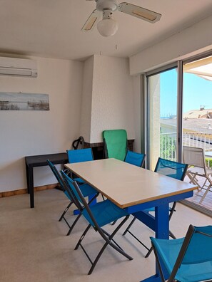 Ein Zimmer mit Tisch, Stühlen, Deckenventilator, Fenster und einem Bild an der Wand.