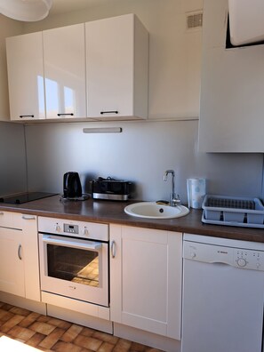 A modern kitchen with white cabinets, a built-in oven, a dishwasher, and a coffee maker. - Between the Sea and Clape: 1st-floor apartment with ocean views, 50 meters from the beach (Narbonne)