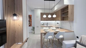 Una cocina moderna con una isla central, iluminación colgante y un área de comedor con sillas blancas.