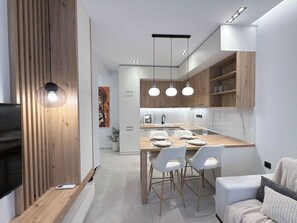 A modern kitchen with a central island, pendant lighting, and a dining area with white chairs. - Stylish City 2BR Apartment | Ad Residences (Thessaloniki)