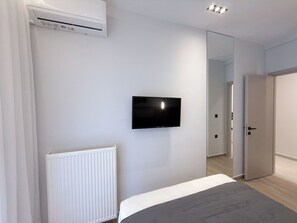 A modern bedroom with a bed, a mounted TV, a radiator, and a door leading to another room. - Stylish City 2BR Apartment | Ad Residences (Thessaloniki)