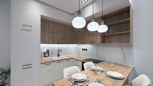 Una cocina moderna con armarios blancos, una mesa de comedor de madera para cuatro personas e iluminación colgante.