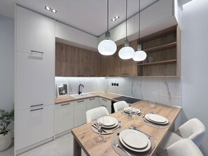 A modern kitchen with white cabinetry, a wooden dining table set for four, and pendant lighting. - Stylish City 2BR Apartment | Ad Residences (Thessaloniki)