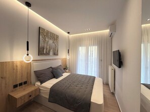 A modern bedroom with a bed, bedside tables, a wall-mounted TV, and a painting. - Stylish City 2BR Apartment | Ad Residences (Thessaloniki)