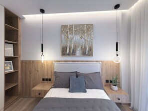 A modern bedroom with a bed, bedside tables, a wall-mounted painting, and pendant lights. - Stylish City 2BR Apartment | Ad Residences (Thessaloniki)