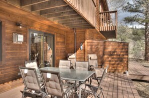 Una terraza de madera con mobiliario exterior y un ventanal que da a un espacio interior.