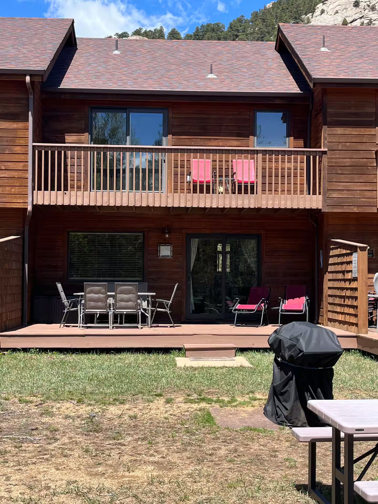 A two-story wooden cabin with a balcony, outdoor seating, and a grill.