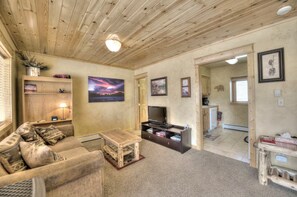 A cozy living room with a wooden ceiling, a sofa, a coffee table, a TV, and a painting. - Bear Creek TWO by Notable Vacation Rentals (Estes Park)