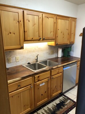 A kitchen with wooden cabinets, a double sink, and a dishwasher. - Bear Creek TWO by Notable Vacation Rentals (Estes Park)
