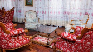 Quarto com duas cadeiras elaboradas, uma mesa de centro de vidro e uma cortina estampada.