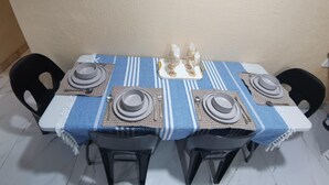 Mesa de jantar posta com pratos, talheres e copos, rodeada por cadeiras.