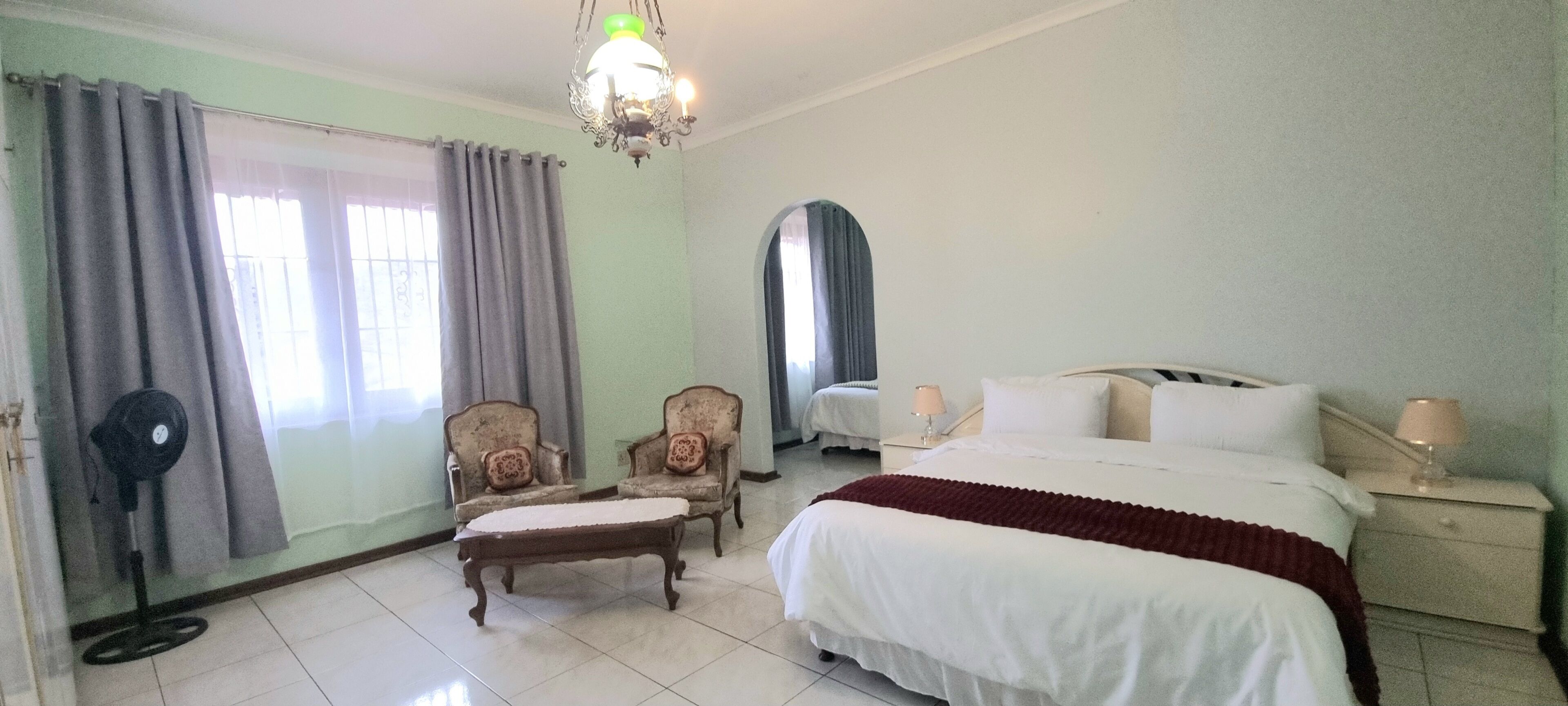 A hotel room with a bed, two armchairs, a small table, a mirror, and a chandelier.