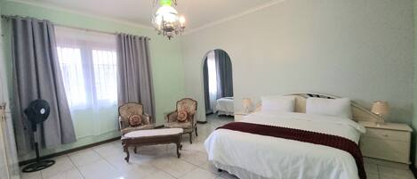 A hotel room with a bed, two armchairs, a small table, a mirror, and a chandelier.