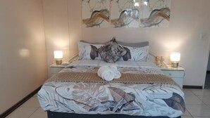 Cama bem arrumada com colcha estampada, duas luminárias de cabeceira e uma obra de arte na parede acima da cama.