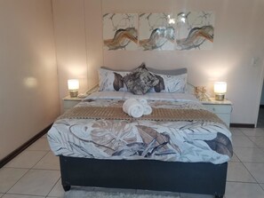 A neatly made bed with a patterned bedspread, two bedside lamps, and a wall-mounted artwork above the bed. - Ojong's Self-Catering Midrand (Midrand)