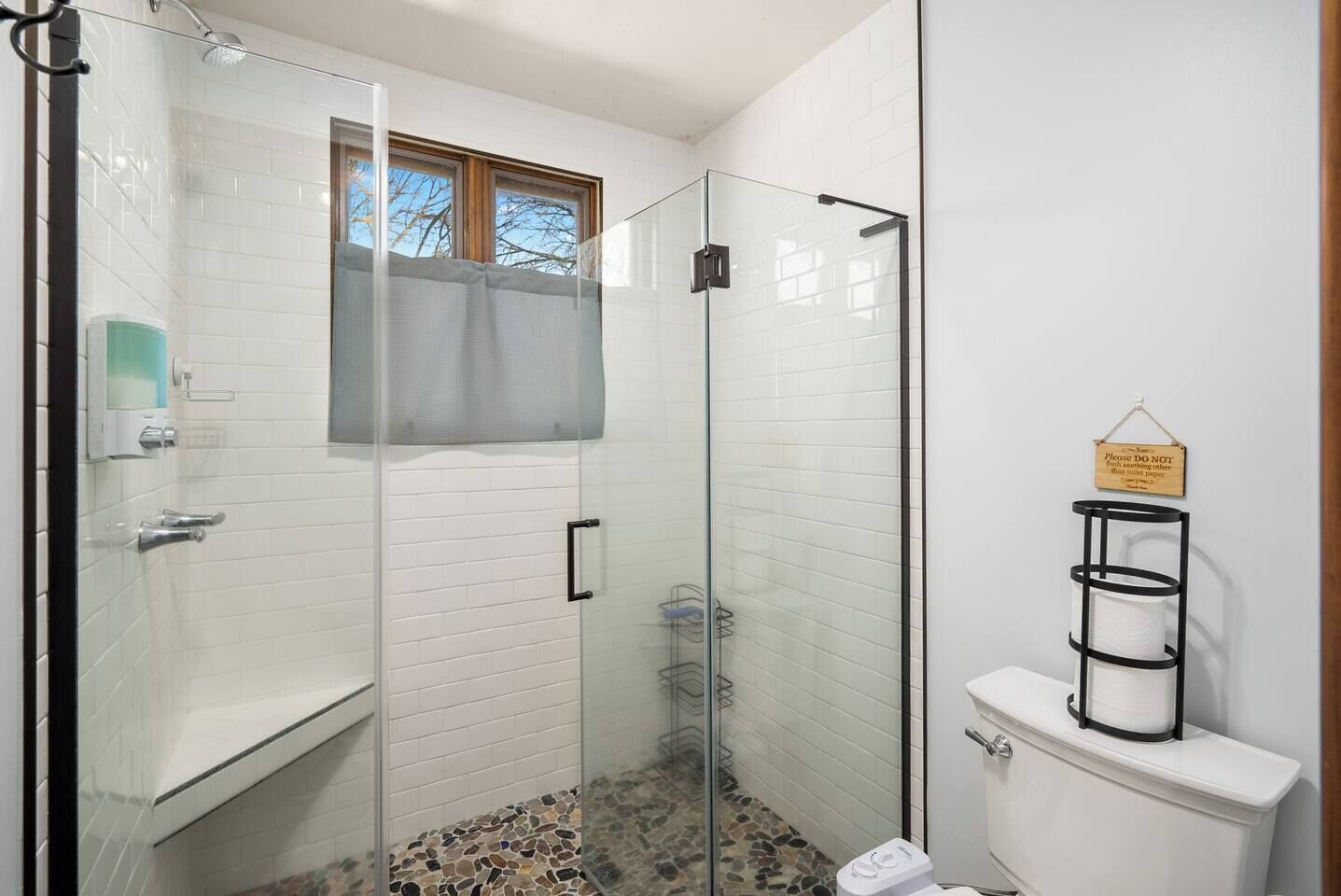 Une salle de bain avec une douche à parois de verre, des toilettes et une étagère avec du papier toilette.