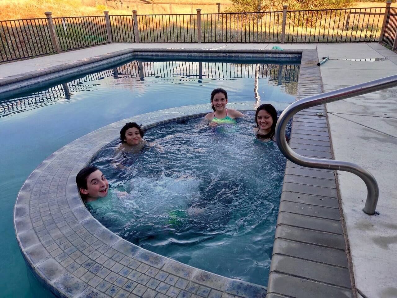A hot tub with four people in it, surrounded by a tiled deck and a metal railing.