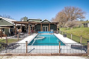 Une piscine rectangulaire avec un jacuzzi, entourée d’une terrasse en bois et d’une clôture en métal.