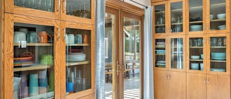 Une cuisine dotée de meubles en bois, d’étagères à portes vitrées et d’une porte-fenêtre coulissante donnant sur un espace extérieur.