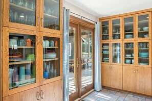 Une cuisine dotée de meubles en bois, d’étagères à portes vitrées et d’une porte-fenêtre coulissante donnant sur un espace extérieur.