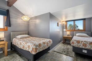 Une chambre avec deux lits, un lustre, une fenêtre donnant sur un beau paysage et une table de chevet en bois.