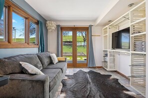 Un salon moderne avec un canapé, un téléviseur et une grande fenêtre donnant sur un jardin.