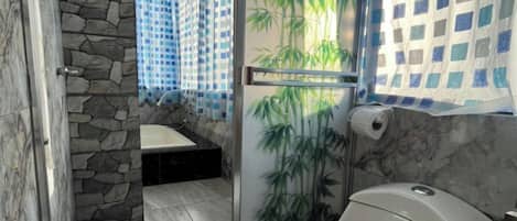 A bathroom with a toilet, a shower with a glass door, and a stone wall.