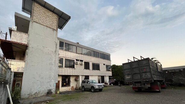 Un edificio de varios pisos con techo plano, un coche estacionado y un camión con un cebra en la parte trasera.