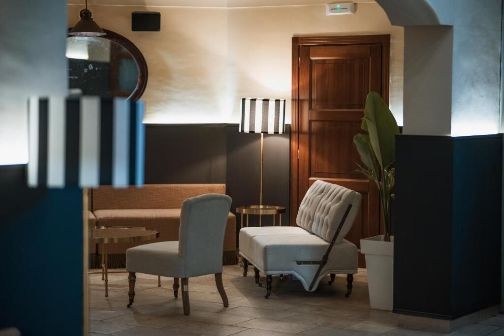 A hotel lobby with a sofa, armchairs, a floor lamp, a potted plant, and a wooden door.