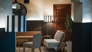 A hotel lobby with a sofa, armchairs, a floor lamp, a potted plant, and a wooden door. - Capomulini Boutique Hotel (Capo Mulini)