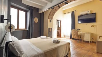 A hotel room with a bed, a desk, a chair, a TV, and an air conditioning unit.