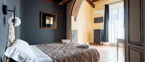 Un dormitorio con cama, espejo, lámpara de pared y ventana con cortinas.