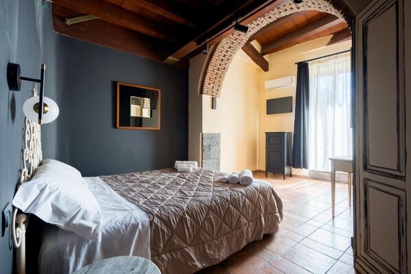 A bedroom with a bed, a mirror, a wall-mounted light fixture, and a window with curtains.
