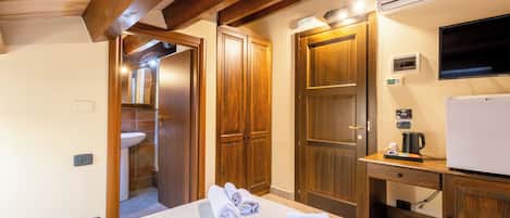 Una habitación de hotel con una cama, un escritorio con hervidor, una televisión y puertas de madera.
