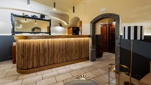 A reception area with a wooden reception desk, a large mirror, and a stone archway. - Capomulini Boutique Hotel (Capo Mulini)