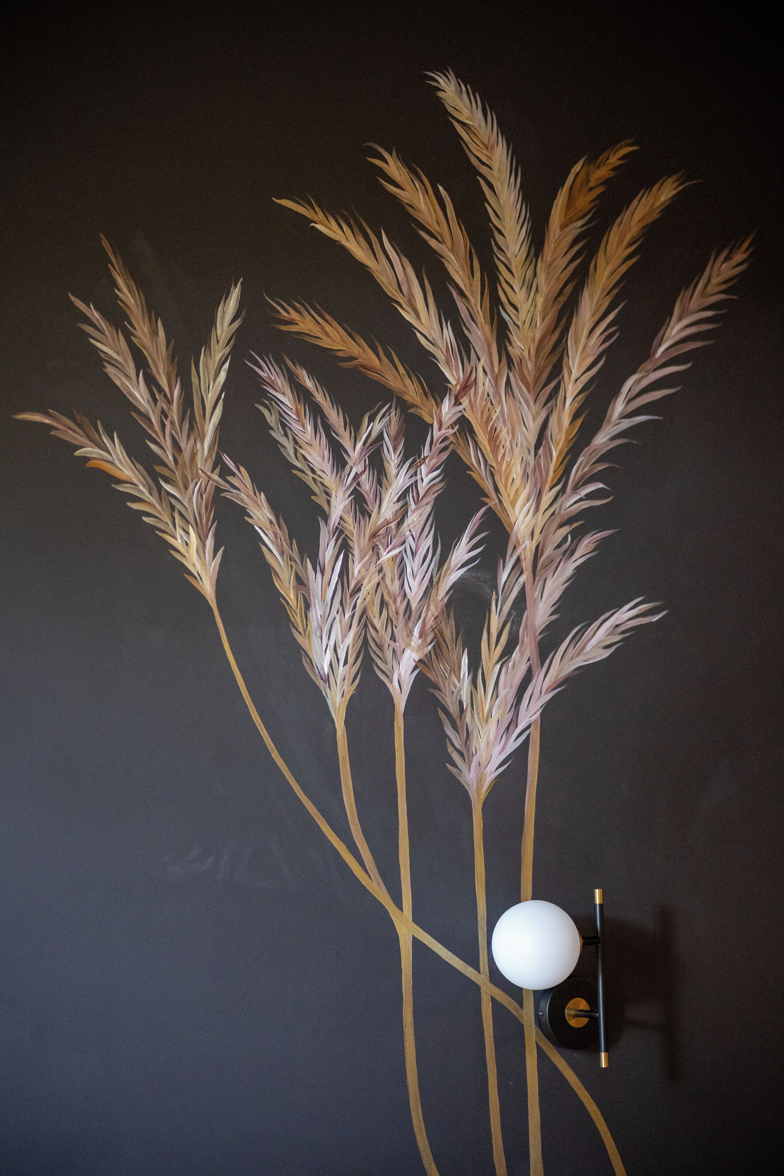 A wall with a decorative arrangement of wheat stalks and a spherical object.