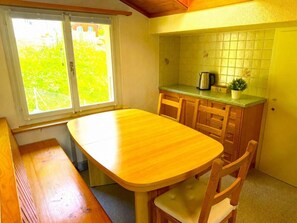 Eine kleine Küche mit Holztisch und -stühlen, einem Fenster mit Aussicht und einer gefliesten Spritzschutzwand.
