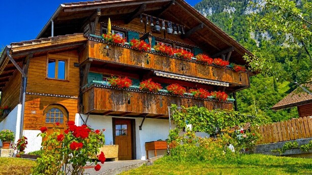 Un chalet traditionnel en bois, doté de plusieurs balcons, d’une porte d’entrée et d’un petit espace porche.