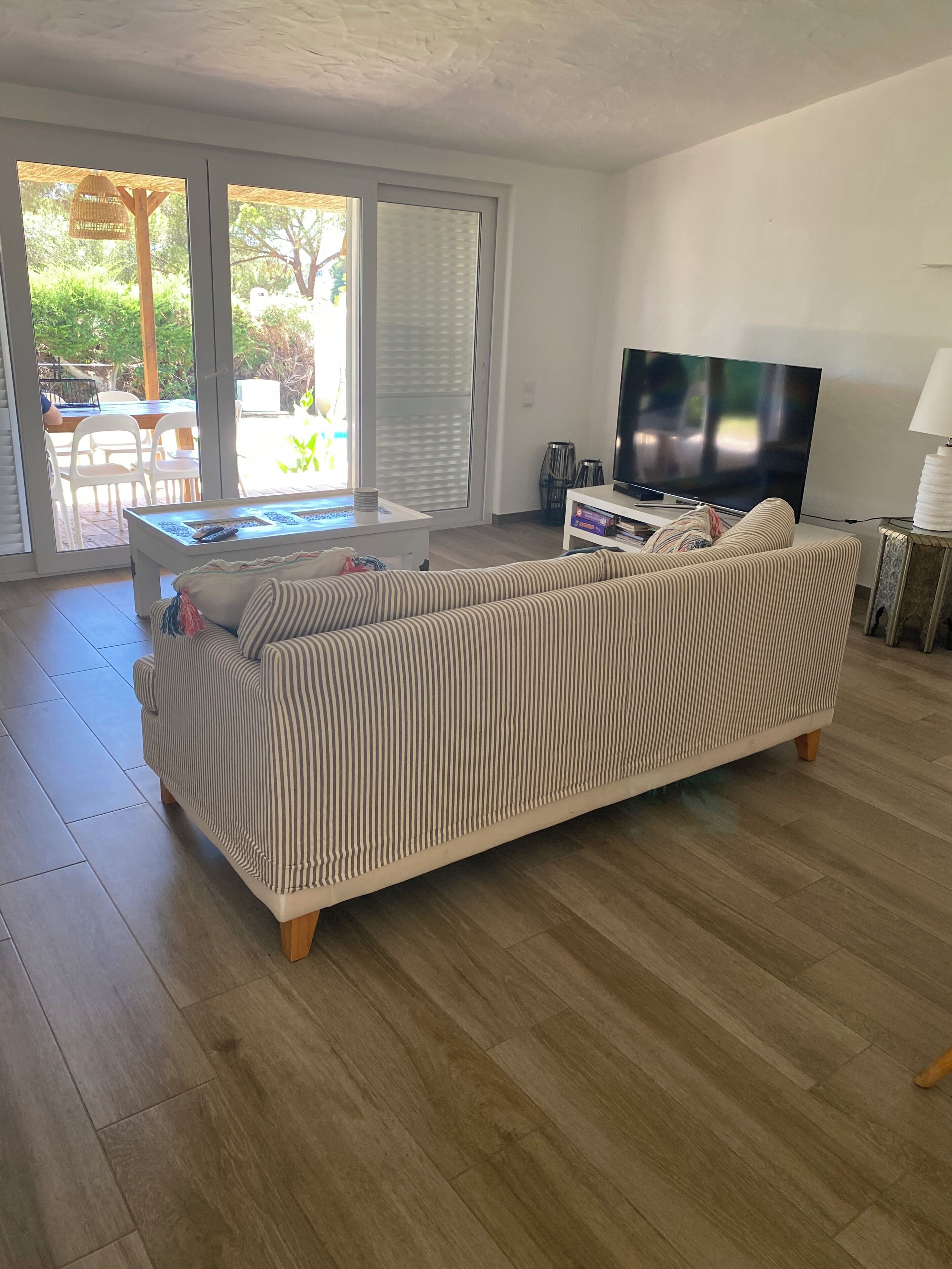 A living room with a striped sofa, a flat-screen TV, and a dining area with chairs and a table.