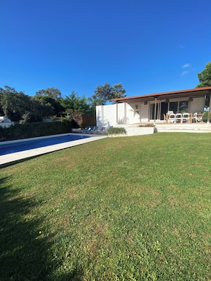 Ein Wohnhaus mit Swimmingpool, einer überdachten Terrasse mit Gartenmöbeln und einem gepflegten Rasen.