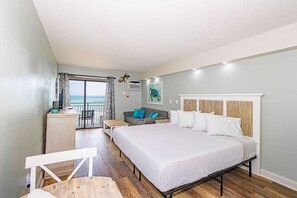 Ein Hotelzimmer mit einem großen Bett, einem Schreibtisch, einem Stuhl, einem Balkon mit Aussicht und einem Bild an der Wand.
