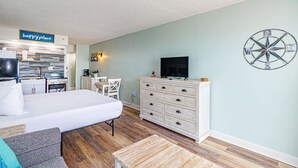 A hotel room with a bed, a dresser, a television, a dartboard, and a kitchen area with a sign that reads 'happy place'. - Sea Mist 20509 Direct Ocean Front Condo (Myrtle Beach)